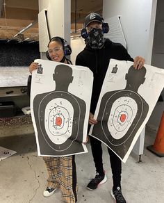 two people standing next to each other holding up posters with darts on them and masks on their faces