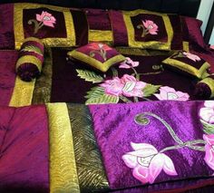 a bed covered in purple and gold sheets with flowers on them, sitting next to a window