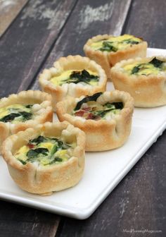 mini quiches with spinach and cheese are on a white plate next to a wooden table