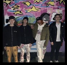 four young men standing next to each other in front of a graffiti wall