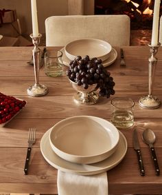 a table set for two with plates, silverware and grapes on the place setting