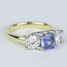 three stone diamond and tan gold ring with an oval blue sapphire surrounded by smaller round diamonds