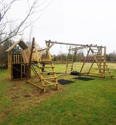 a wooden play set in the middle of a grassy area with swings and ladders