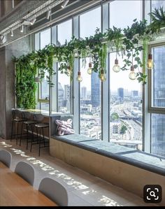 an office with large windows and plants growing on the wall, along with long tables and chairs