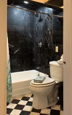 a white toilet sitting next to a black and white checkered bath tub in a bathroom