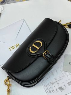 The Dior Bobby East-West bag is a modern version of the hobo style, characterized by graceful lines and harmonious proportions. The black chrome calfskin design is complemented by soft suede lining and aged gold tone metal hardware. Featuring a detachable, adjustable sliding strap with a signature military-style buckle, the Dior Bobby Bag can be carried in hand, over the shoulder or comfortably over the shoulder. Dimensions: 22 x 13 x 5 cm. Dior Bobby Bag, Bobby East, Bobby Bag, Hobo Style, Black Chrome, How To Make Handbags, Purses Designer, East West, Bags Designer Fashion