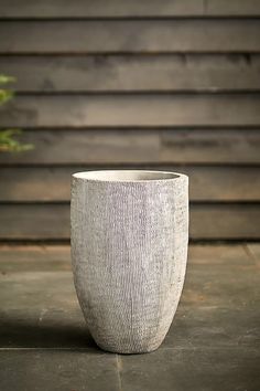 a white vase sitting on top of a wooden floor next to a plant in front of a building