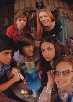 a group of young people standing around a table with a blue vase on top of it