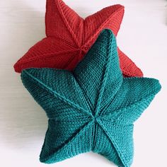 two red and green knitted stars sitting on top of a white table next to each other