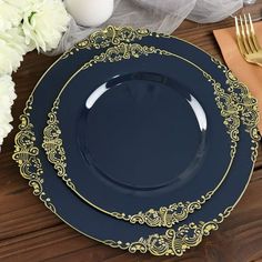 two blue plates with gold trim sit on a wooden table next to white flowers and silverware