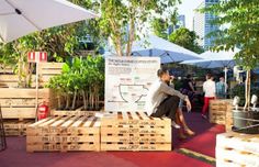 a man sitting on top of wooden pallets in front of trees and people standing around