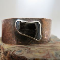 Elevate your style with our handmade Petrified Wood in Copper Cuff bracelet. The unique polished black stone with white detailing at the edges adds a touch of sophistication to any outfit. The cuff is 7/8" wide, from a 6" piece of copper, and the stone is 3/4" x 1/2." The cuff is adjustable and the edges are rounded for wearability and comfort. Artisan Black Bangle Jewelry, Handmade Black Cuff Bracelet, Artisan Adjustable Black Cuff Bracelet, Unique Black Bangle Cuff Bracelet, Rustic Black Bracelets As A Gift, Rustic Black Bracelets As Gift, Rustic Black Bracelet For Gift, Rustic Black Bracelet Perfect For Gifting, Unique Black Cuff Bracelets