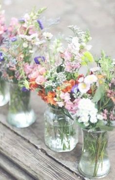 four glass vases filled with colorful flowers on top of a wooden table next to a bench