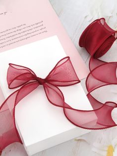 a white box with a red ribbon on top of it next to flowers and a card