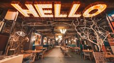 the inside of a restaurant with wooden tables and chairs in front of a neon sign that reads hello