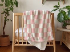 a pink and white checkered blanket sitting on top of a wooden crib next to a potted plant