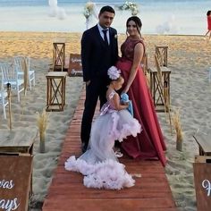 a man and woman standing on a wooden walkway at the beach with chairs set up in front of them