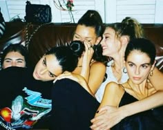 four women sitting on a couch with their arms around each other and one woman covering her face