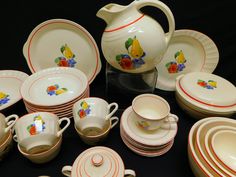 a table topped with lots of white and red dishes next to a vase filled with fruit