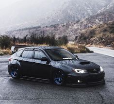 the black car is parked on the side of the road in front of some mountains