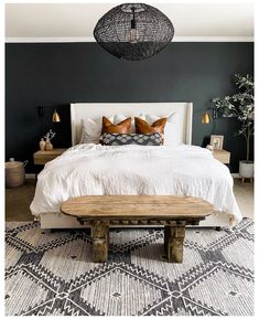 a bedroom with black walls, white bedding and wooden bench in the middle of the room