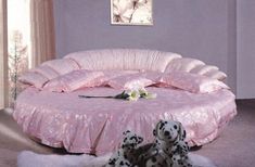 a dog laying on the floor in front of a round bed with pink sheets and pillows