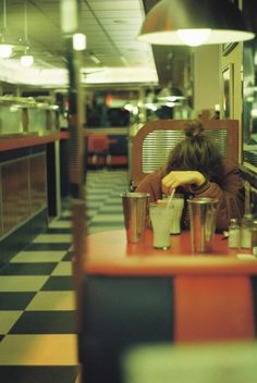 a woman sitting at a table in a restaurant with food on the counter and chairs