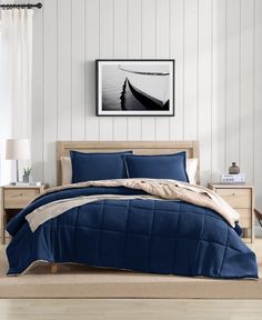 a bed with blue comforter and pillows in a room next to a painting on the wall