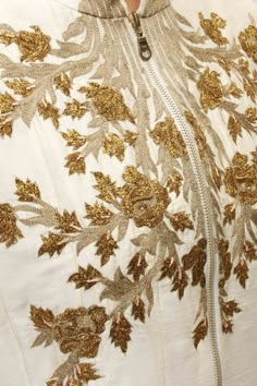 a close up of a woman wearing a white dress with gold embroidered flowers on it