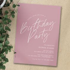 a pink birthday party card sitting on top of a table next to a potted plant