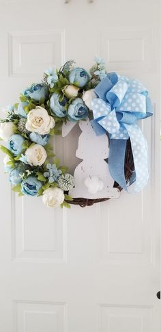 a wreath with blue and white flowers hanging on the front door is decorated with an easter bunny