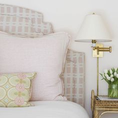 a white bed topped with pillows and a lamp next to a table filled with flowers