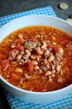 a white bowl filled with chili and beans on top of a blue checkered cloth