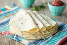 a stack of tortilla sitting on top of a table next to a bowl of salsa