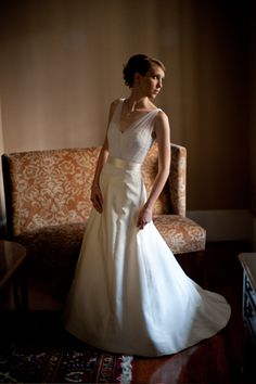 a woman in a white wedding dress standing next to a couch and chair with her hands on her hips