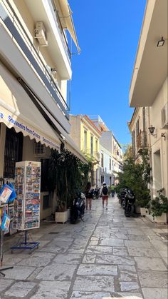 people are walking down the street in front of shops and buildings on a sunny day