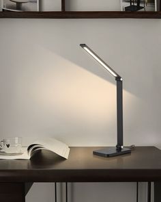 a desk lamp on top of a wooden table next to a book and coffee cup