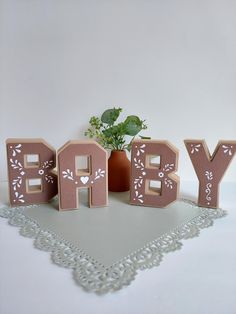 wooden letters spelling the word baby next to a potted plant on a doily