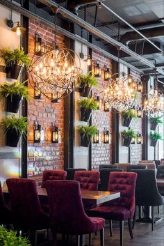 a restaurant with brick walls and chandeliers hanging from it's ceiling, surrounded by potted plants