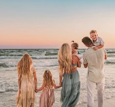 a family walking on the beach at sunset with one child holding his mom's shoulders