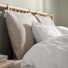 a bed with white linens and pillows on it's headboard, next to a window