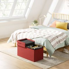 a bedroom with white walls and wooden flooring has a bed, nightstands, and red storage box