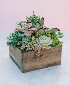 a wooden box filled with succulents on top of a white tablecloth