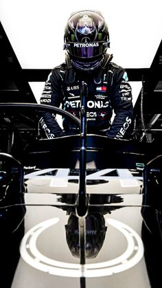 a man sitting in front of a car on top of a race track with the reflection of his helmet