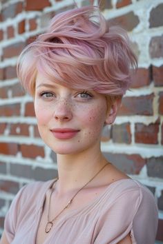 Young woman with pink hair styled in an updo, freckles, smiling at the camera in front of a brick wall. Widow's Peak