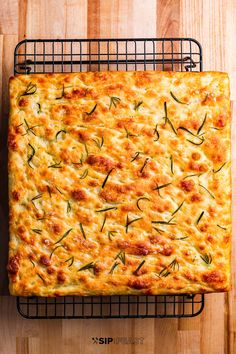 a square casserole with cheese and green onions on a wire rack next to a wooden table