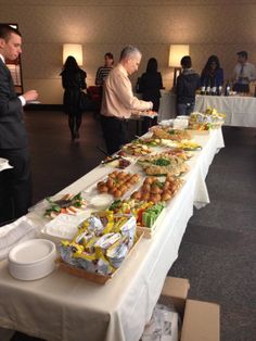 people are standing around a long table with food on it