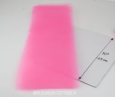 a pair of scissors and a piece of pink fabric on a white table with a ruler