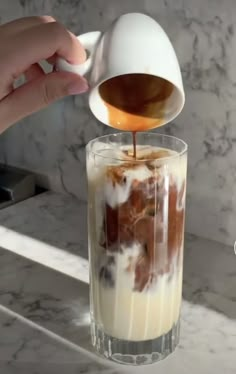 someone is pouring something into a glass with ice cream and caramel in it on a marble counter top