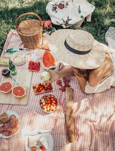 a woman in a straw hat sitting at a picnic table with fruit and bread on it